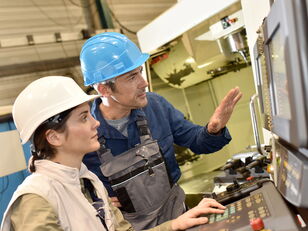 Mann und Frau mit Arbeitsschutzhelm vor Steuerpult