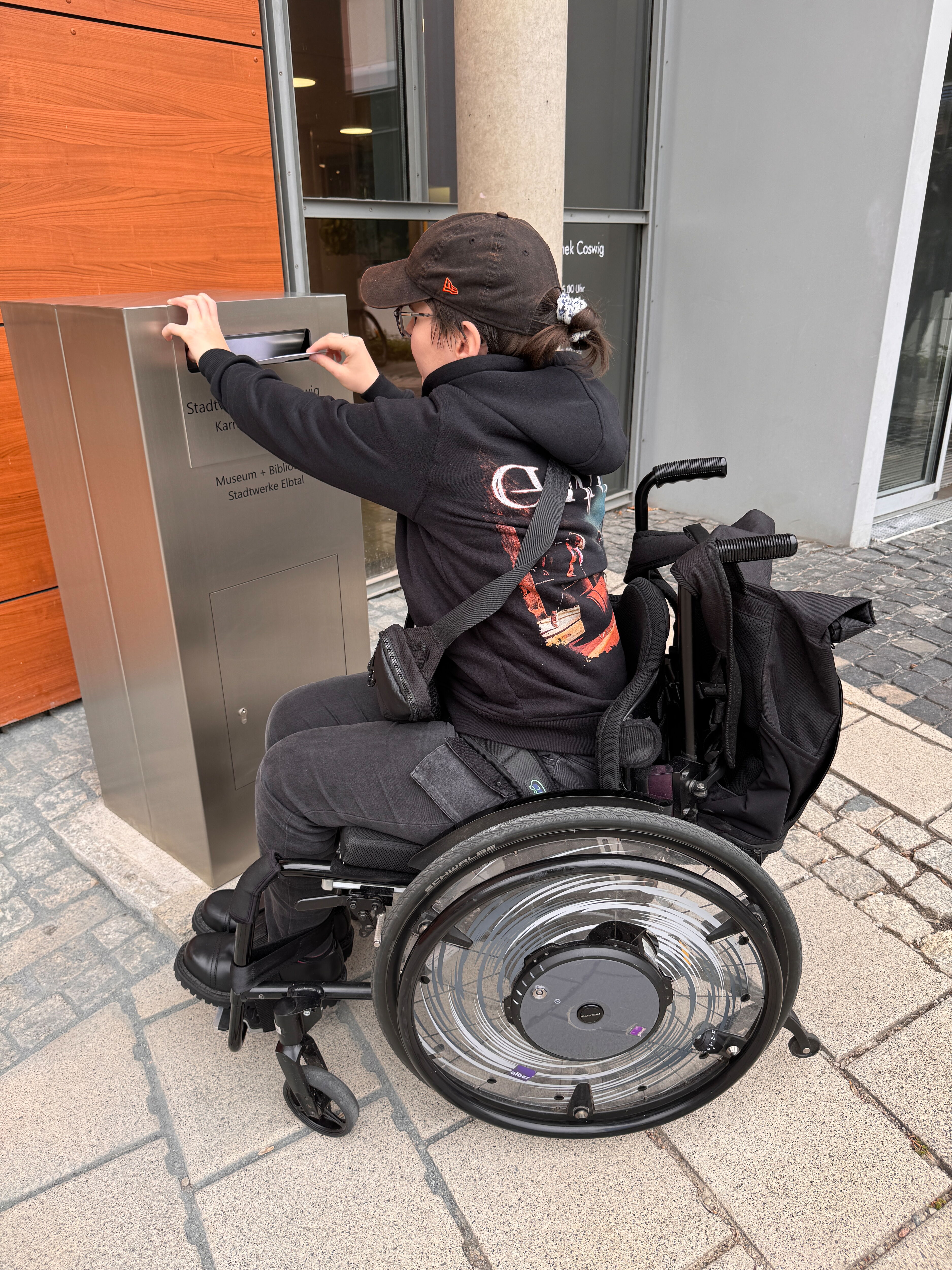 Rollstuhlfahrerin wirft in den neuen Briefkasten einen Brief ein.
